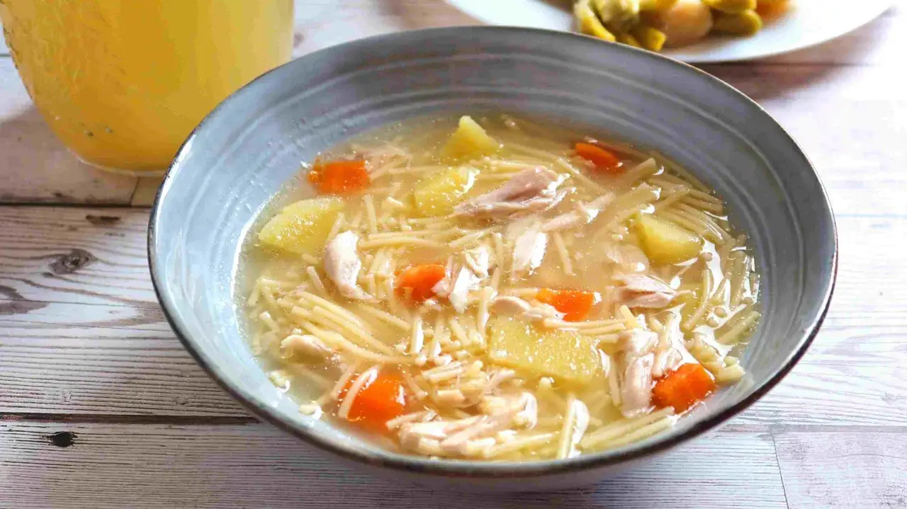 Un reconfortante plato de sopa de pollo con fideos finos, trozos de zanahoria y patata, y hebras de pollo desmenuzado.