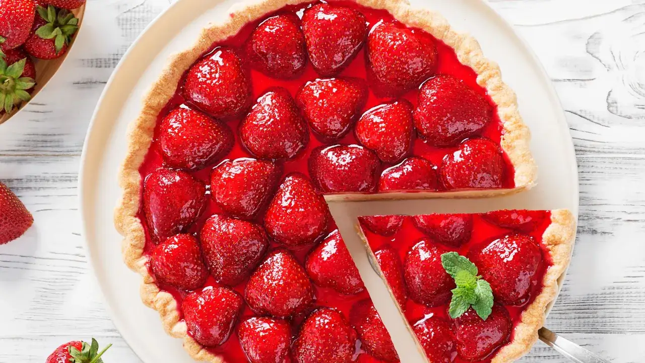Deliciosa tarta de fresas cubierta con gelatina brillante y fresas frescas. Una porción se ha cortado, revelando la jugosa fruta.