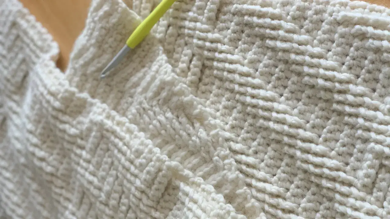 Tejido blanco con patr&oacute;n de espiga y un ganchillo listo para hacer un punto deslizado.