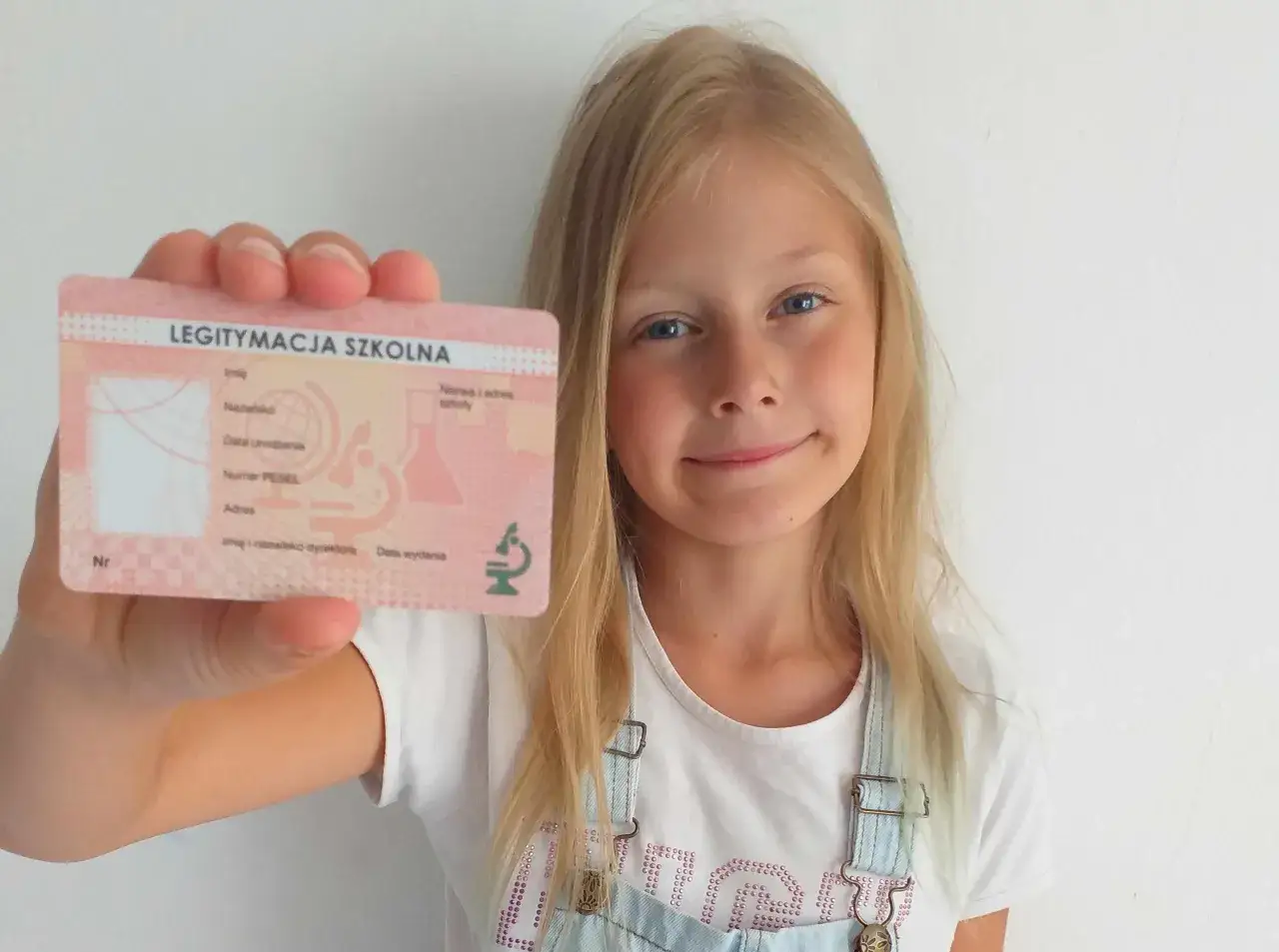 Uśmiechnięta dziewczynka pokazuje legitymację szkolną.
