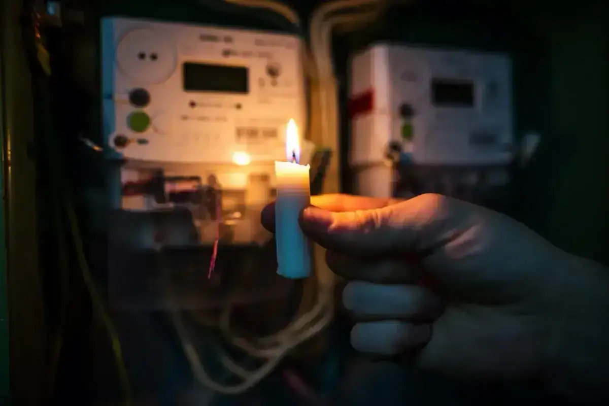 Gdy najemca nie płaci czynszu, można odłączyć mu media. Płonąca świeca w dłoni na tle liczników energii elektrycznej symbolizuje brak prądu.