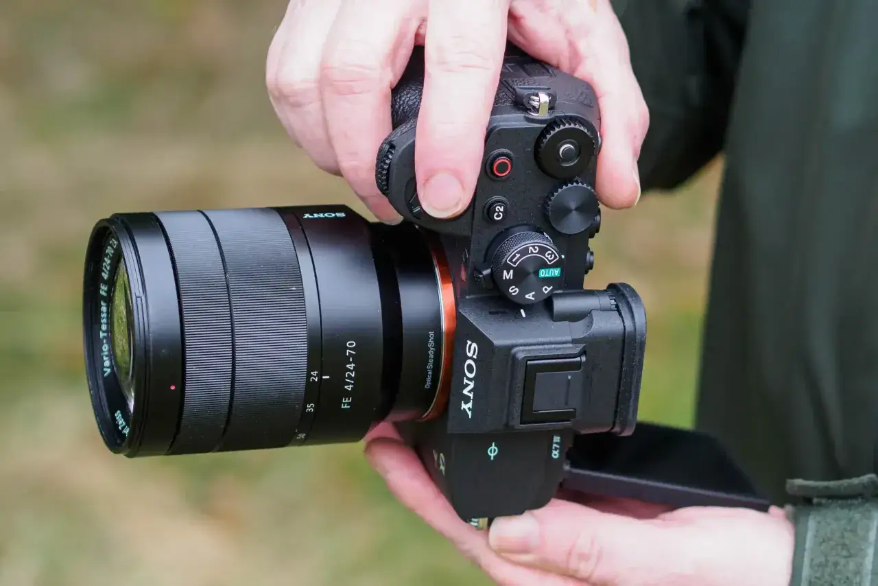 Dłonie trzymają aparat Sony a7 IV z obiektywem Vario-Tessar 24-70mm. Testowanie sprzętu w plenerze.