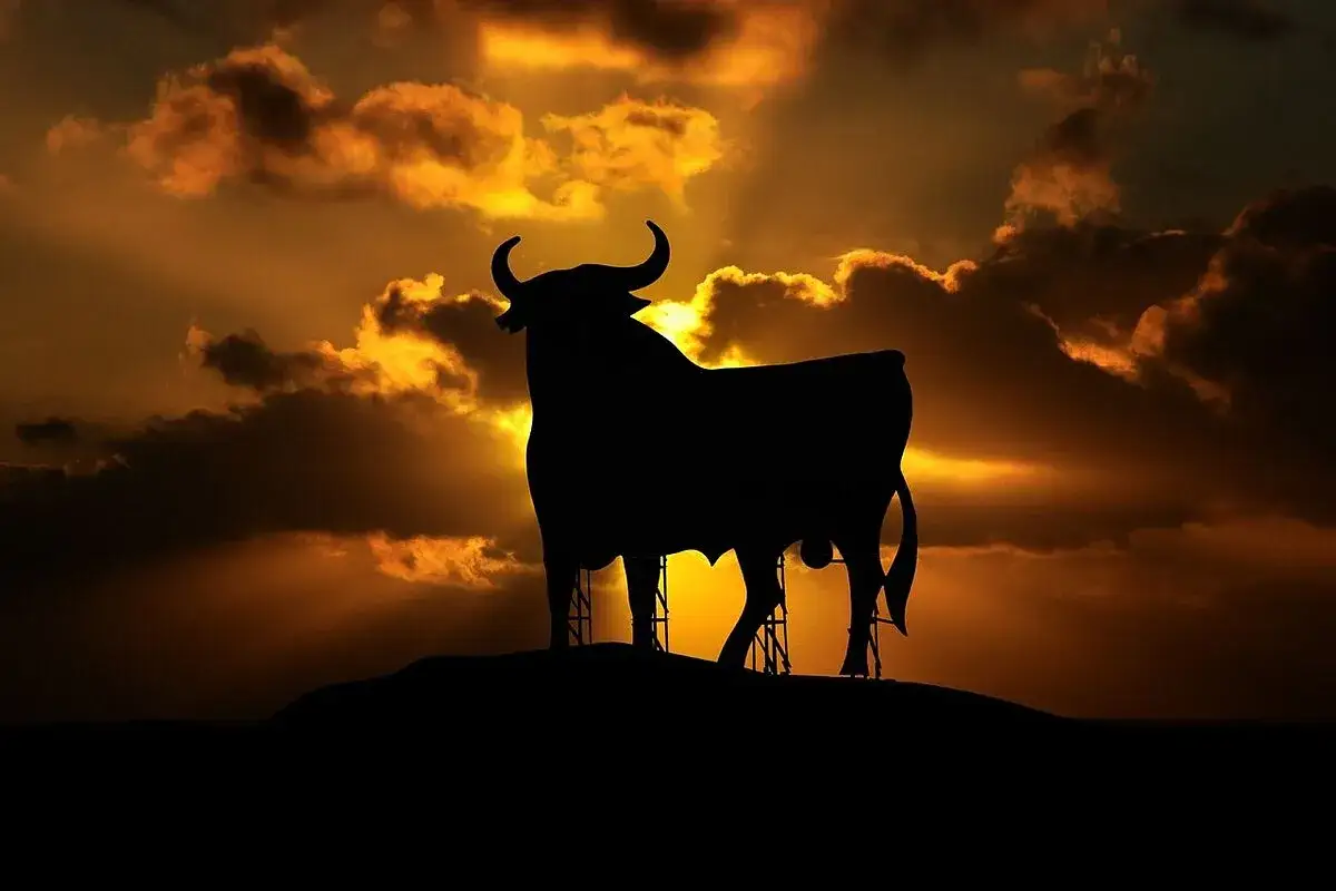 Silueta de un toro imponente contra un atardecer dramático. Reflexiona sobre qué significa soñar con toros: fuerza, pasión o desafíos.