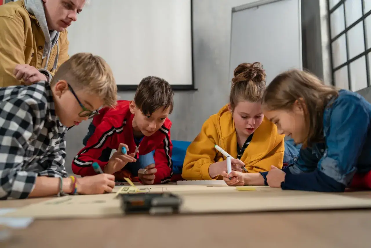 Grupa dzieci pracuje nad projektem, a trener umiejętności społecznych wspiera ich pracę.