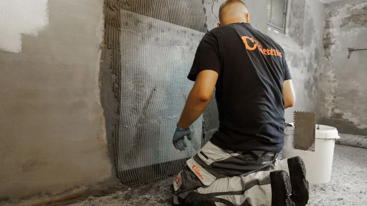 Handwerker trägt Bitumenanstrich innen auf Wand auf, verstärkt mit Gewebe.