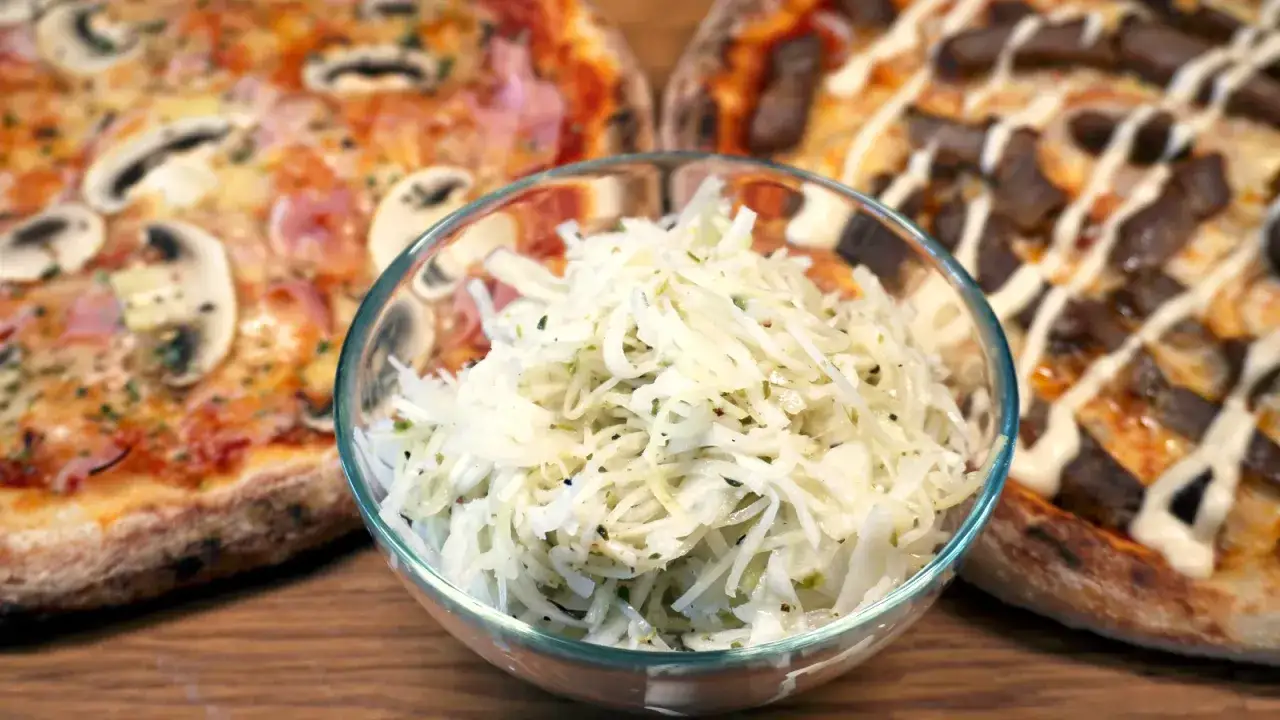 En skål med pizzasallad, en klassiker med okänt pizzasallad ursprung, står framför två läckra pizzor.