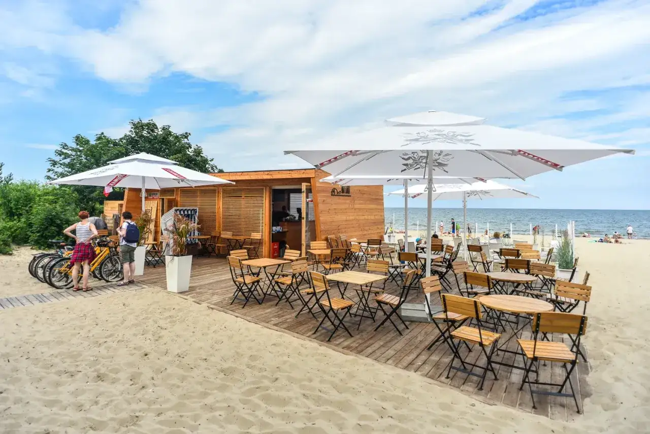 Drewniana plażowa kawiarnia z parasolami i stolikami, idealne miejsce na relaks. To jedne z najlepszych restauracji w Sopocie.