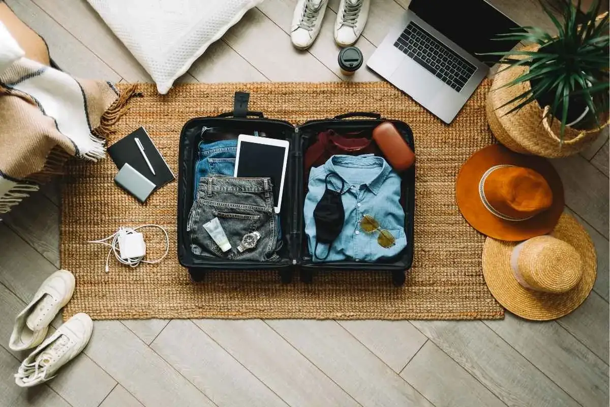 Przygotowujesz się do wyjazdu? Oto lista rzeczy, co zabrać na wakacje: walizka z ubraniami, tablet, buty, czapki, laptop i akcesoria.