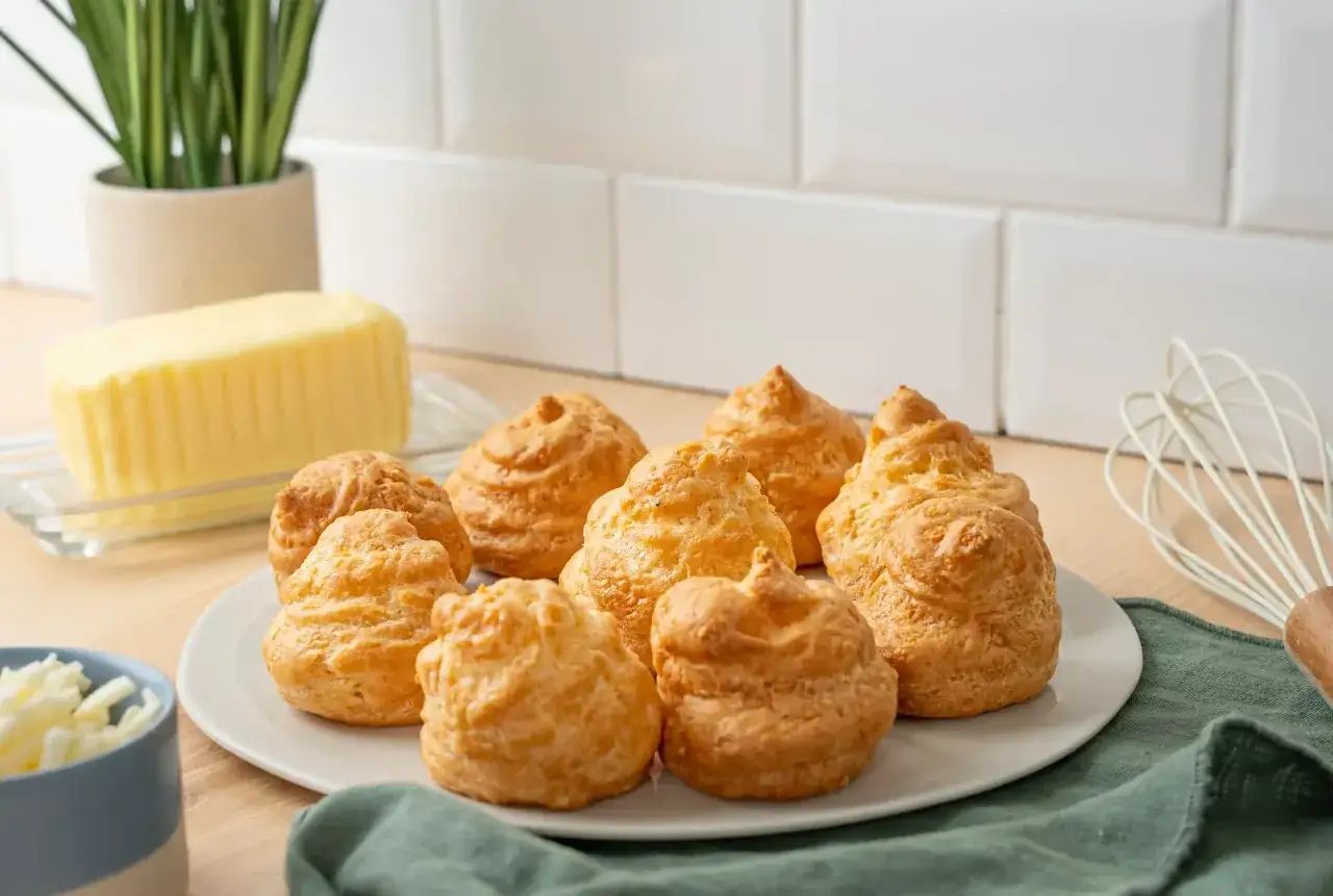 Une assiette de goug&egrave;res au fromage dor&eacute;es, avec du beurre et du fromage r&acirc;p&eacute; &agrave; proximit&eacute;.