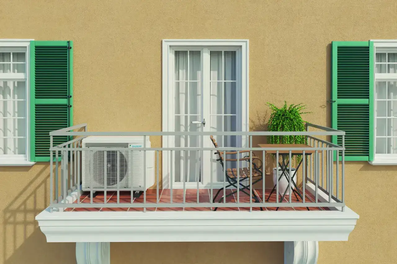 Balkon eines Mehrfamilienhauses mit Klimaanlage, Tisch und Stuhl. Grüne Fensterläden und eine Tür mit Vorhängen.