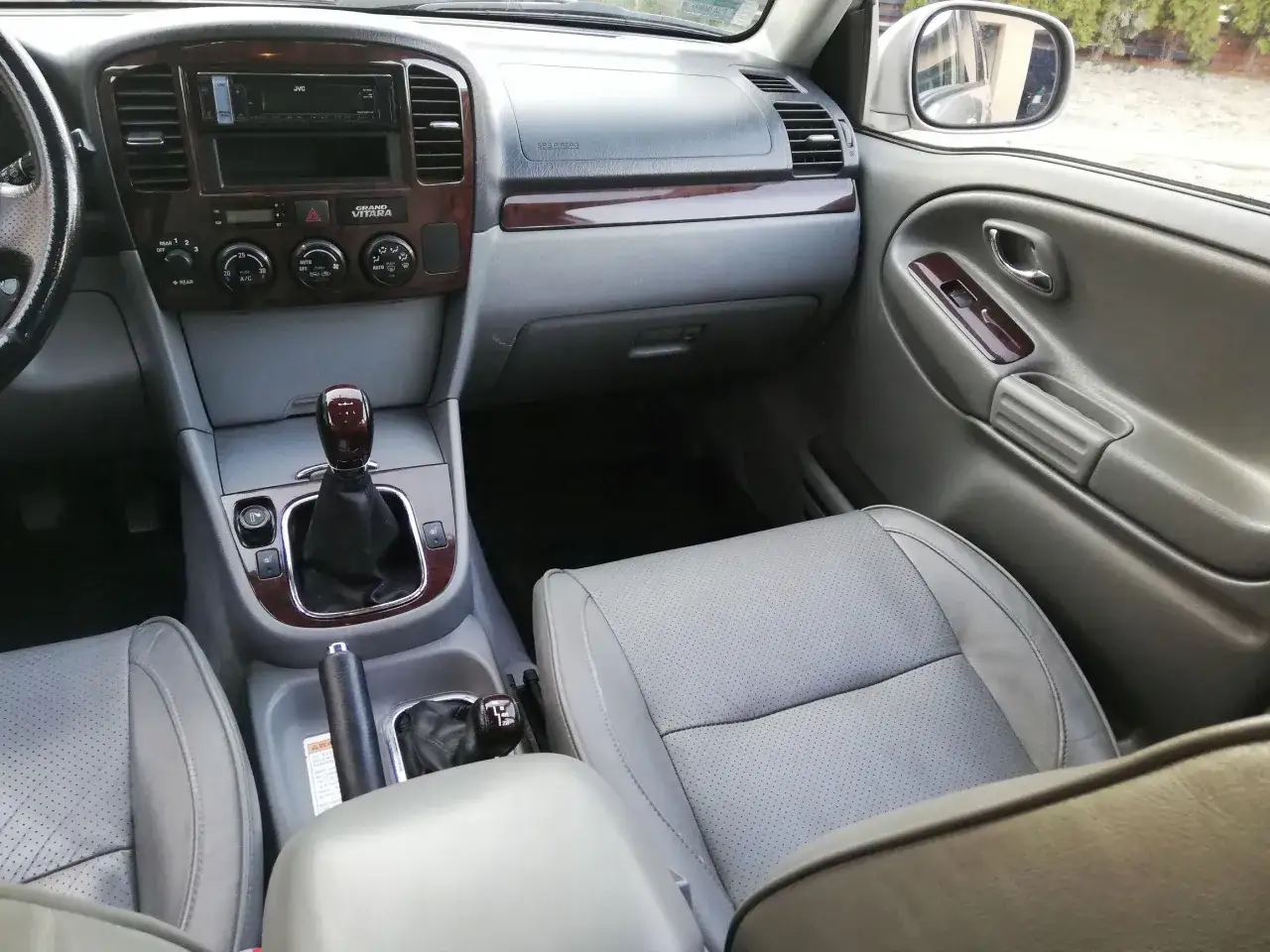 Wnętrze Suzuki XL7 z szarą skórzaną tapicerką, drewnianymi wstawkami i automatyczną skrzynią biegów.