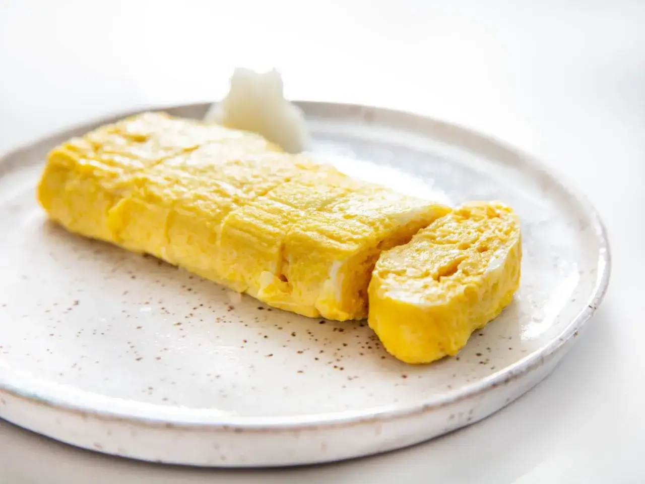 Złocisty omlet do sushi, pokrojony na kawałki, prezentuje się apetycznie na talerzu.