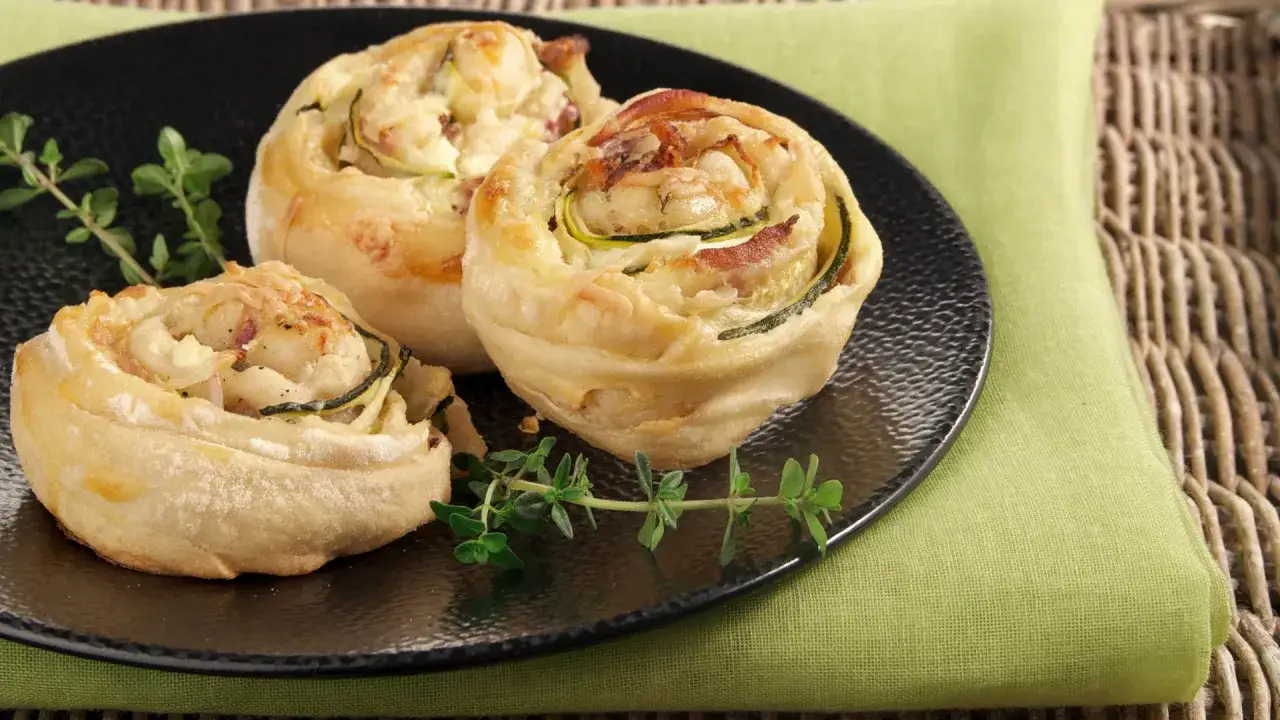 Drei goldbraune zucchini schnecken mit Käse und Kräutern auf schwarzer Platte.