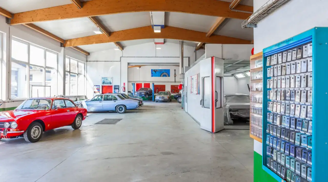Werkstatt mit Oldtimern, bereit für die **Oldtimer Lackierung**. Ein roter Alfa Romeo und weitere Klassiker warten auf frische Farbe.