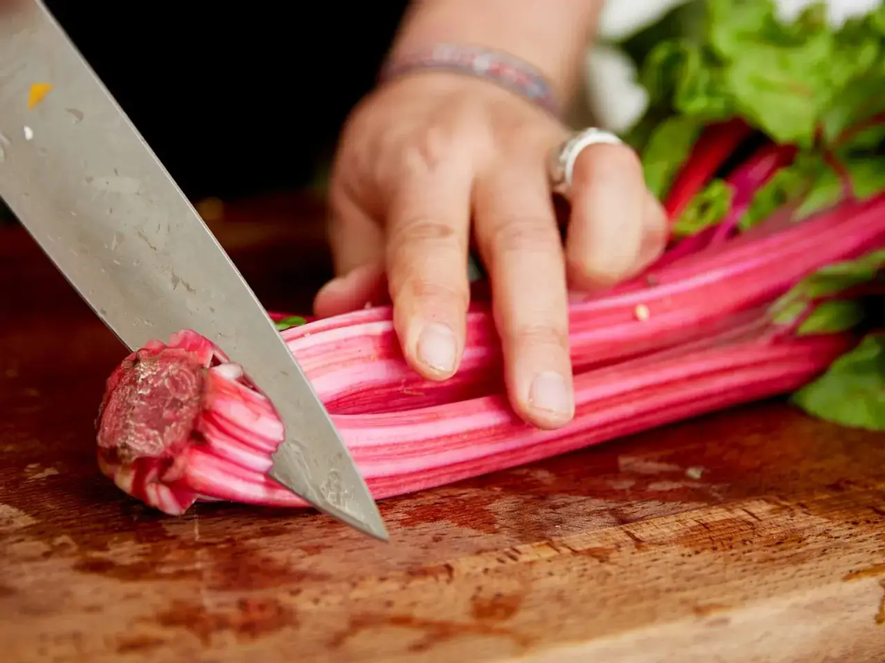 Hand schneidet rote Mangoldstiele für leckere Mangold Rezepte auf einem Holzbrett.