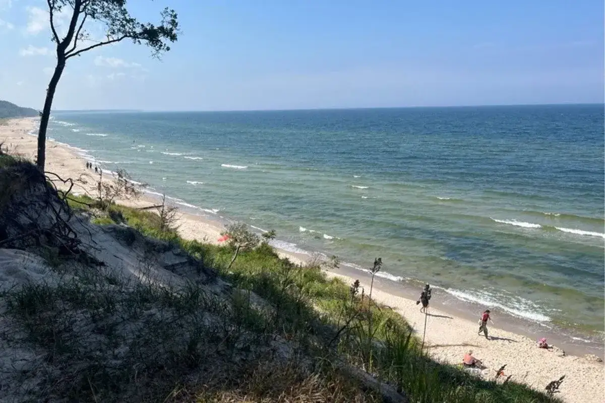 Piękne plaże nad morzem, z piaszczystym wybrzeżem i łagodnymi falami. Kilka osób spaceruje i odpoczywa na piasku.