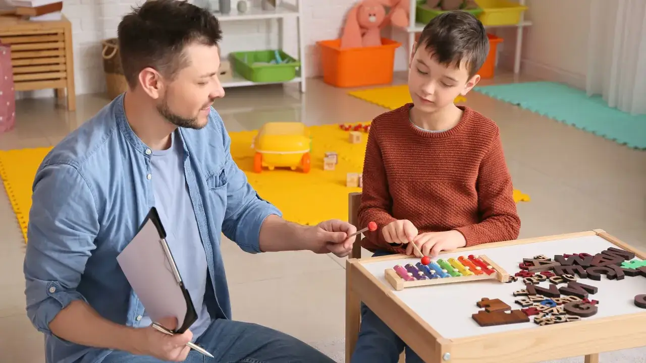 Un terapista aiuta un bambino con asperger a suonare uno xilofono. La terapia &egrave; fondamentale per capire cos'&egrave; l'asperger.