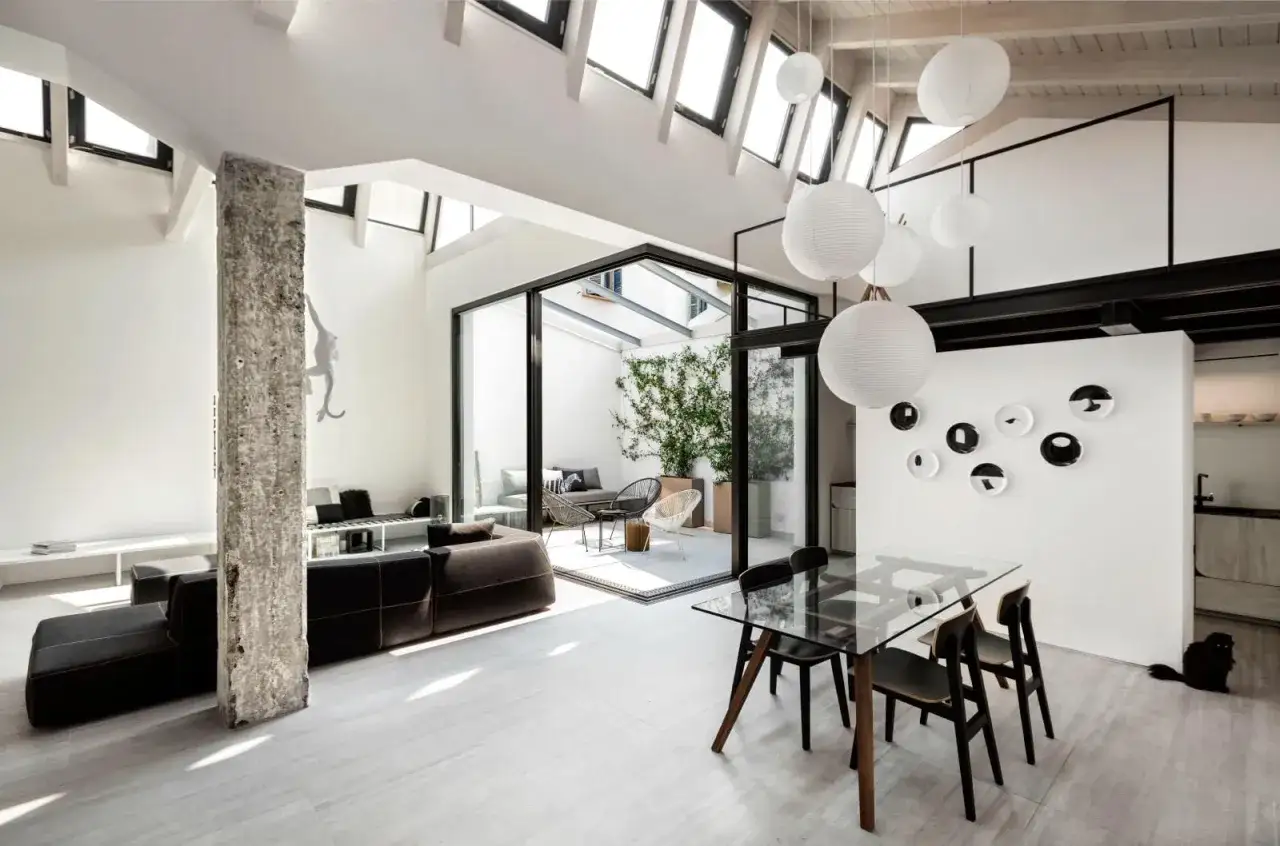 Un loft con altillo moderno y luminoso, con sofás oscuros, mesa de cristal y un patio interior. Ideas para espacios abiertos.