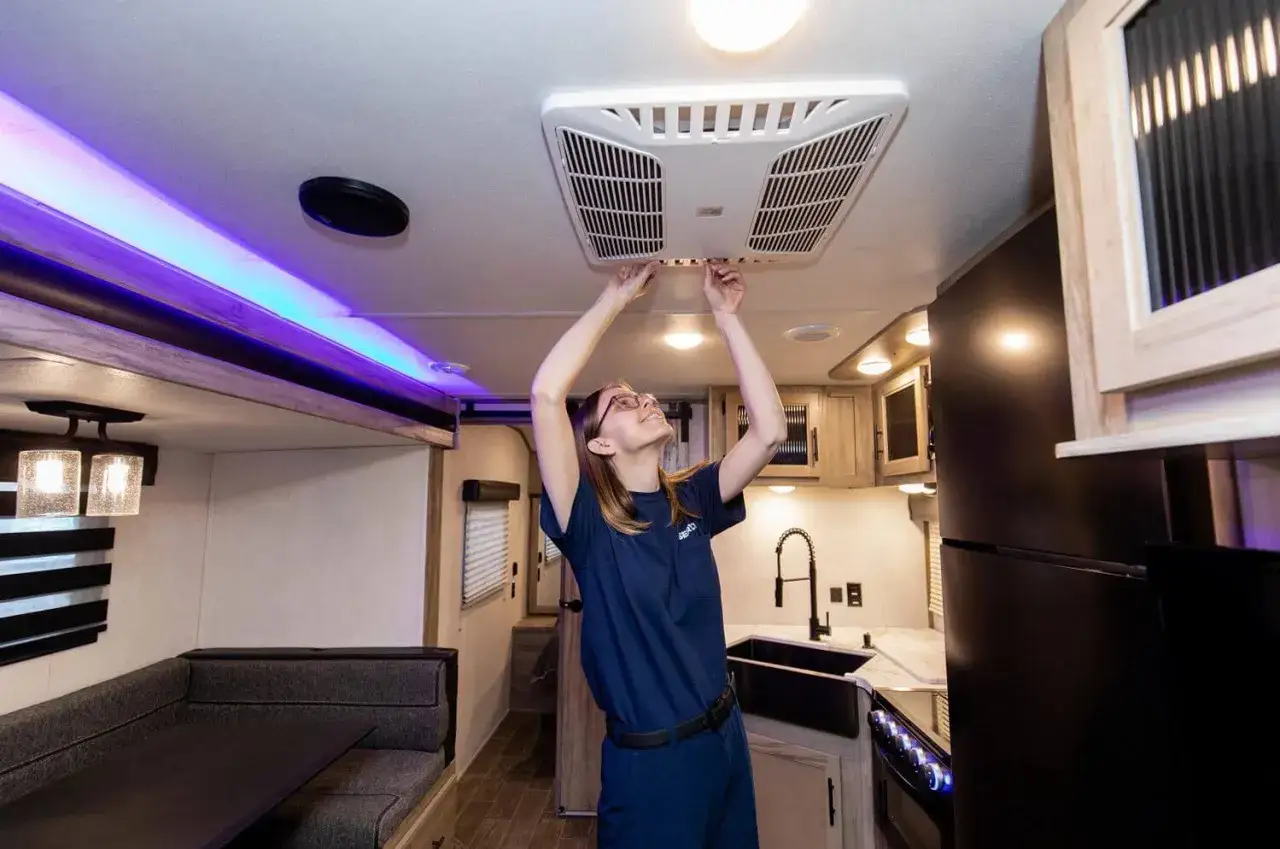 Une femme ajuste le climatiseur de son camping-car, assurant un confort optimal pour ses voyages.