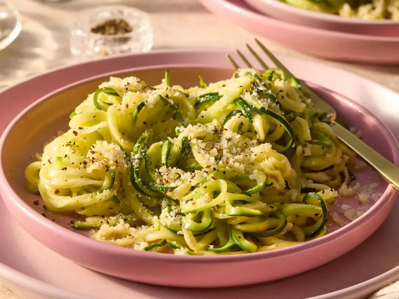 Ein Teller mit Zoodles, garniert mit geriebenem Käse und Pfeffer. Ein einfaches und gesundes Zoodles Rezept für jeden Tag.