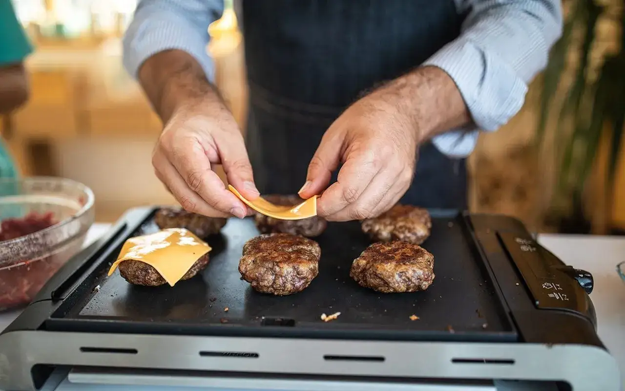 Jak grillować na grillu elektrycznym? Ręce kładą ser na grillowanych kotletach.