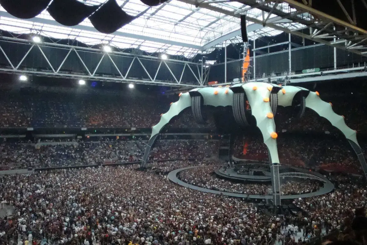 Koncert znanych zespołów muzycznych zagranicznych w ogromnym tłumie na stadionie. Spektakularna scena w kształcie pająka.