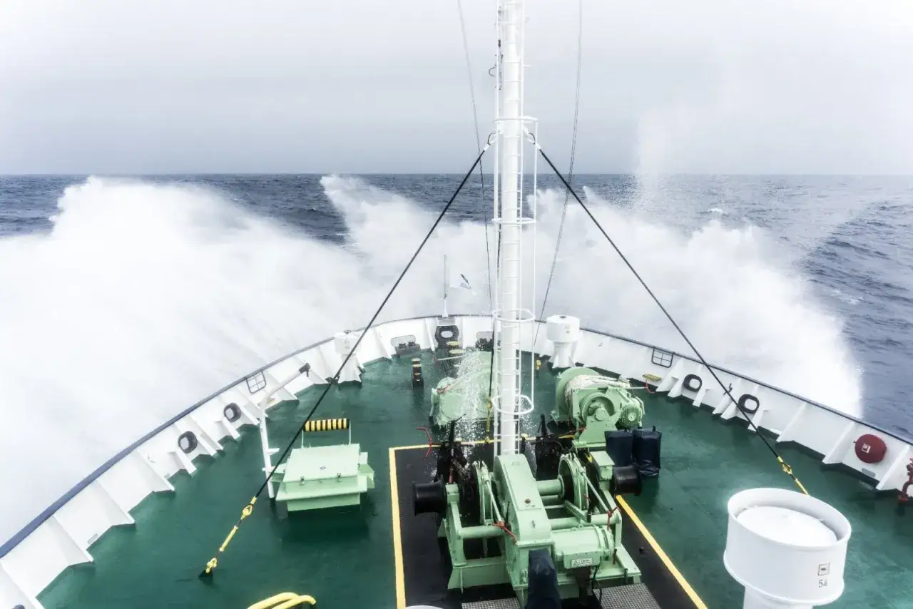 Olas rompen contra el barco en el paso de Drake. El mar agitado salpica la cubierta con maquinaria verde.