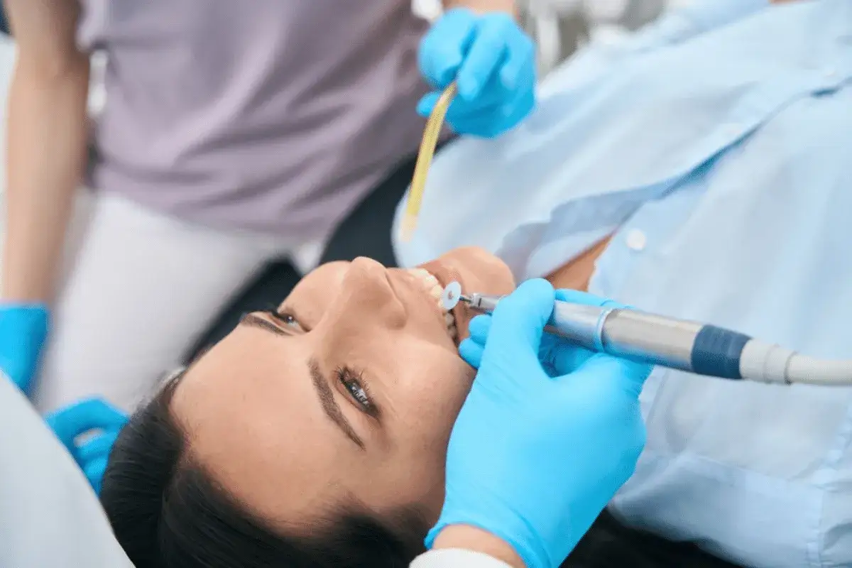 Dentysta wykonuje zabieg stomatologiczny, stosując opatrunek na zęba. Pacjentka leży na fotelu, a dentysta używa wiertła.