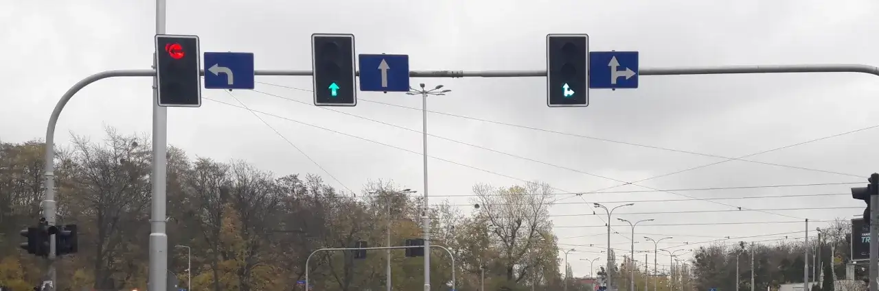 Sygnalizacja świetlna: czerwone światło dla skrętu w lewo, zielone dla jazdy prosto i zielone dla jazdy prosto i w prawo. Znak S3 informuje o dopuszczonych kierunkach jazdy.