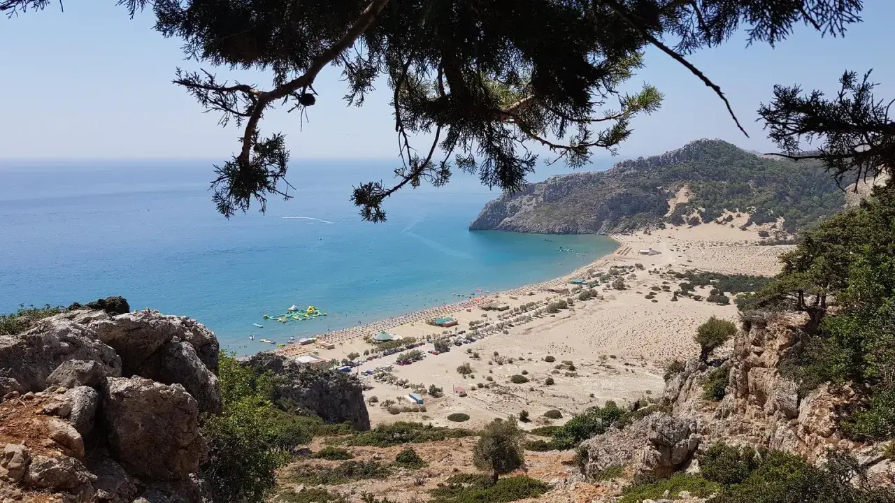 Widok na Tsambika Beach z góry: piaszczysta plaża, turkusowe morze, leżaki, parasole i wodny plac zabaw.