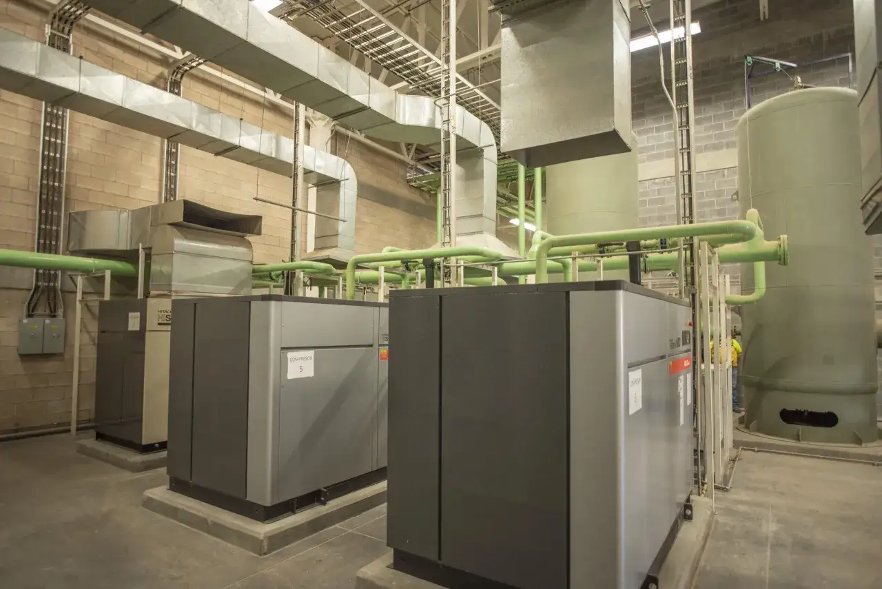 Sala de compresores con equipos de alta tecnología, incluyendo varios compresores Gimenez, tuberías verdes y tanques de almacenamiento.