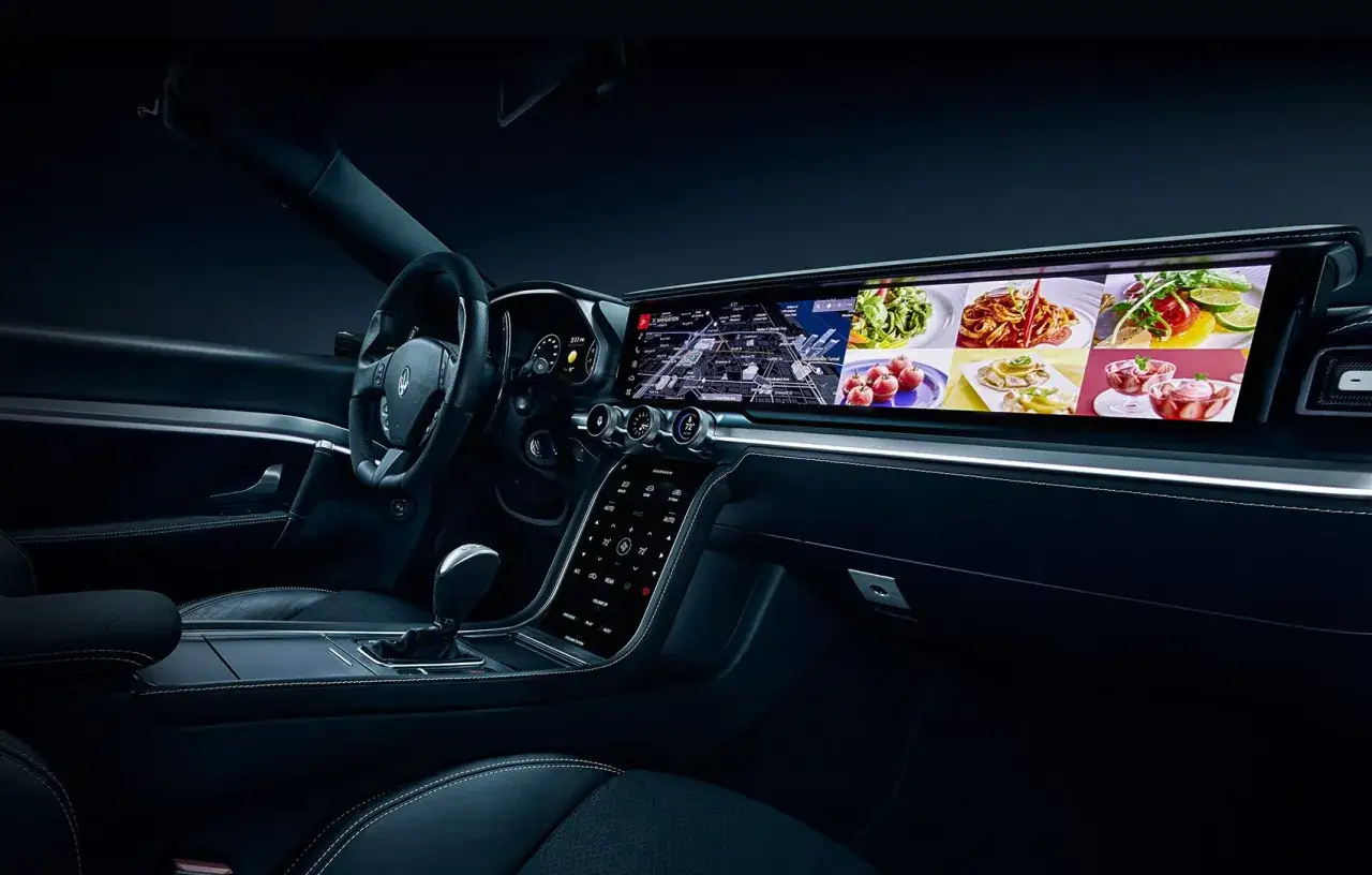 Interno auto con volante, cambio e un ampio schermo che mostra un virtual cockpit con navigazione e immagini di cibo.