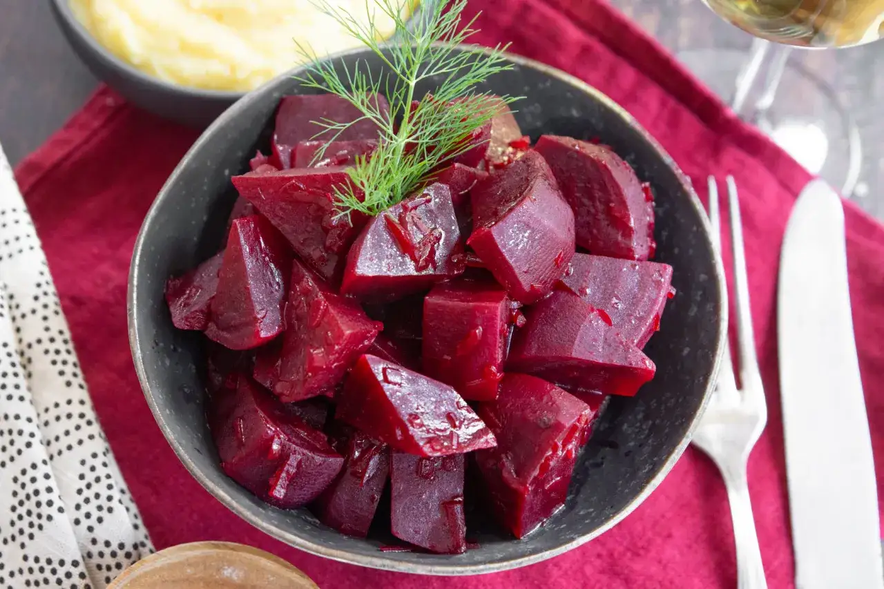 Sch&uuml;ssel mit gew&uuml;rfelten roten Bete, die man roh essen kann, garniert mit Dill. Daneben Kartoffelp&uuml;ree, Besteck und ein Weinglas.