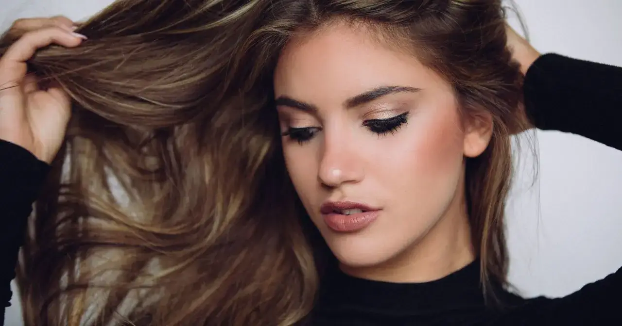 Chica con cabello castaño largo y ondulado, ojos maquillados con delineado cat eye y labios nude. Un ejemplo de trucos de belleza para un look natural.