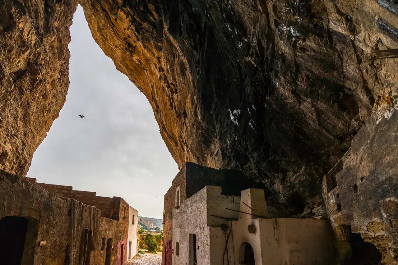 Antica grotta mangiapane con case scavate nella roccia e un uccello in volo nel cielo.