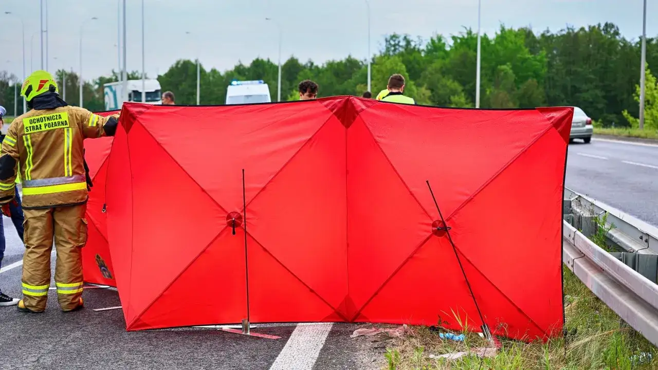 Czerwony parawan przy wypadku oznacza, że służby zabezpieczają miejsce zdarzenia. Strażak w mundurze stoi obok.