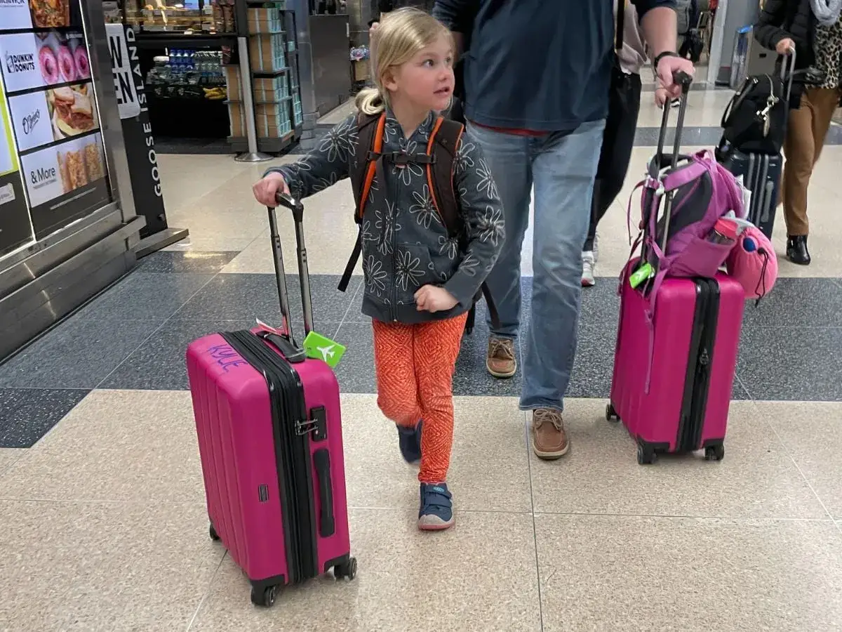 Ein kleines M&auml;dchen mit einem Rucksack und einem pinken Koffer, bereit f&uuml;r eine 