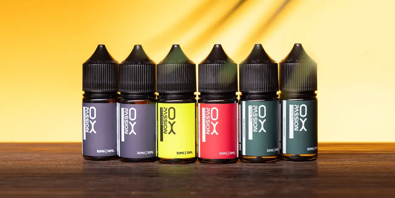 Seis botellas de e-juice de la marca OX PASSION, con diferentes sabores y concentraciones de nicotina, dispuestas en fila sobre una superficie de madera.