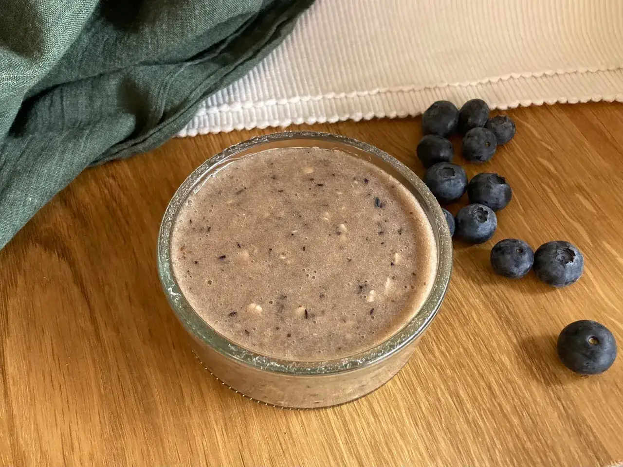Ein Glas cremiger Heidelbeeren-Brei, perfekt für jedes Baby. Frische Heidelbeeren liegen daneben.