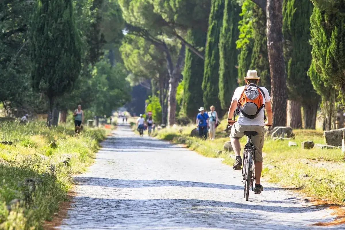 Un homme &agrave; v&eacute;lo explore la voie Appienne, un site historique pr&egrave;s de Rome, entour&eacute; de cypr&egrave;s et de ruines antiques.