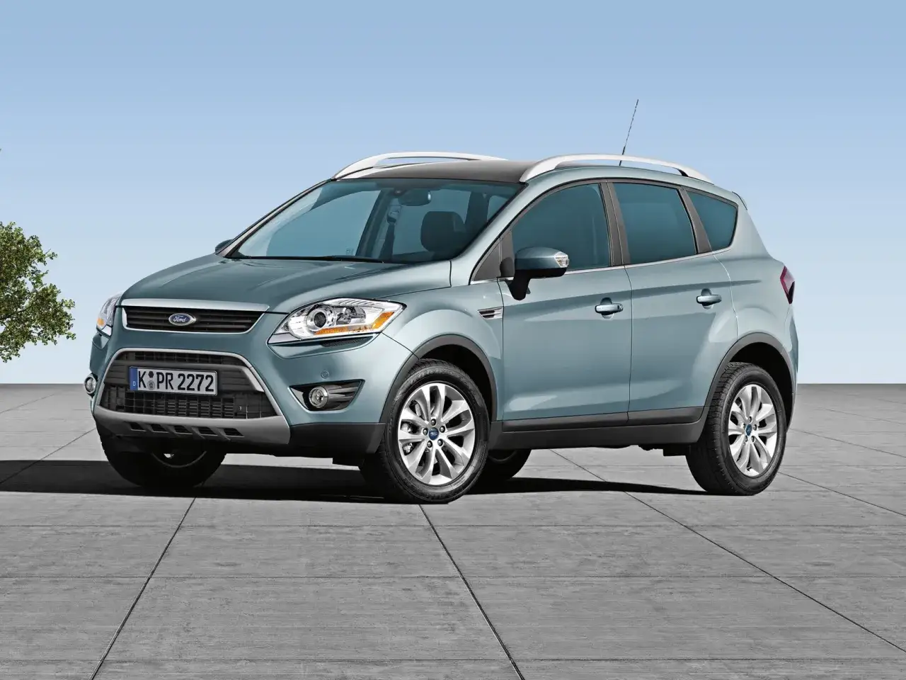 Niebieski Ford Kuga, idealny SUV do 30 tys. zł, z relingami dachowymi i felgami aluminiowymi, stoi na betonowym placu.