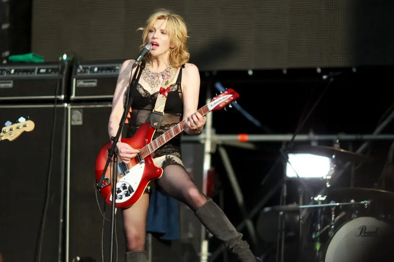Une icône du punk des années 90, une guitariste blonde, micro en main, joue sur scène avec passion.