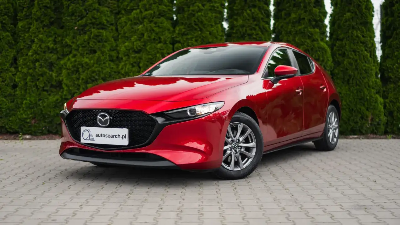 Czerwona Mazda 3 Skyactiv, zaparkowana przed żywopłotem, prezentuje swoje eleganckie linie.
