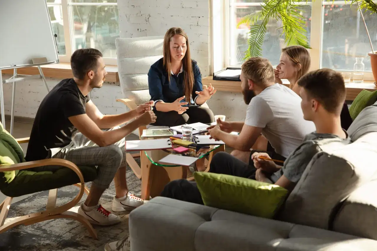 Grupp diskuterar idéer kring likhetsprincipen brf. En kvinna leder samtalet, medan andra lyssnar och antecknar.
