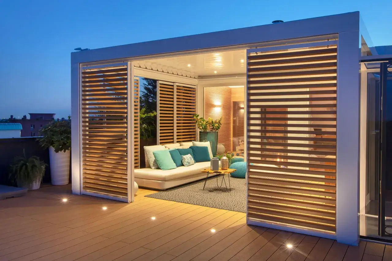 Un moderno spazio esterno con divano, tavolino e pouf, illuminato da luci soffuse. Ideale per costruire una pergola accogliente.