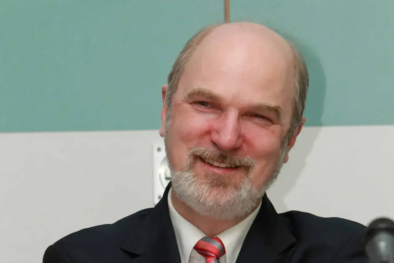 Ein Mann mit Glatze und Bart, Thomas Schirrmacher, lächelt in die Kamera. Er trägt einen dunklen Anzug und eine Krawatte.