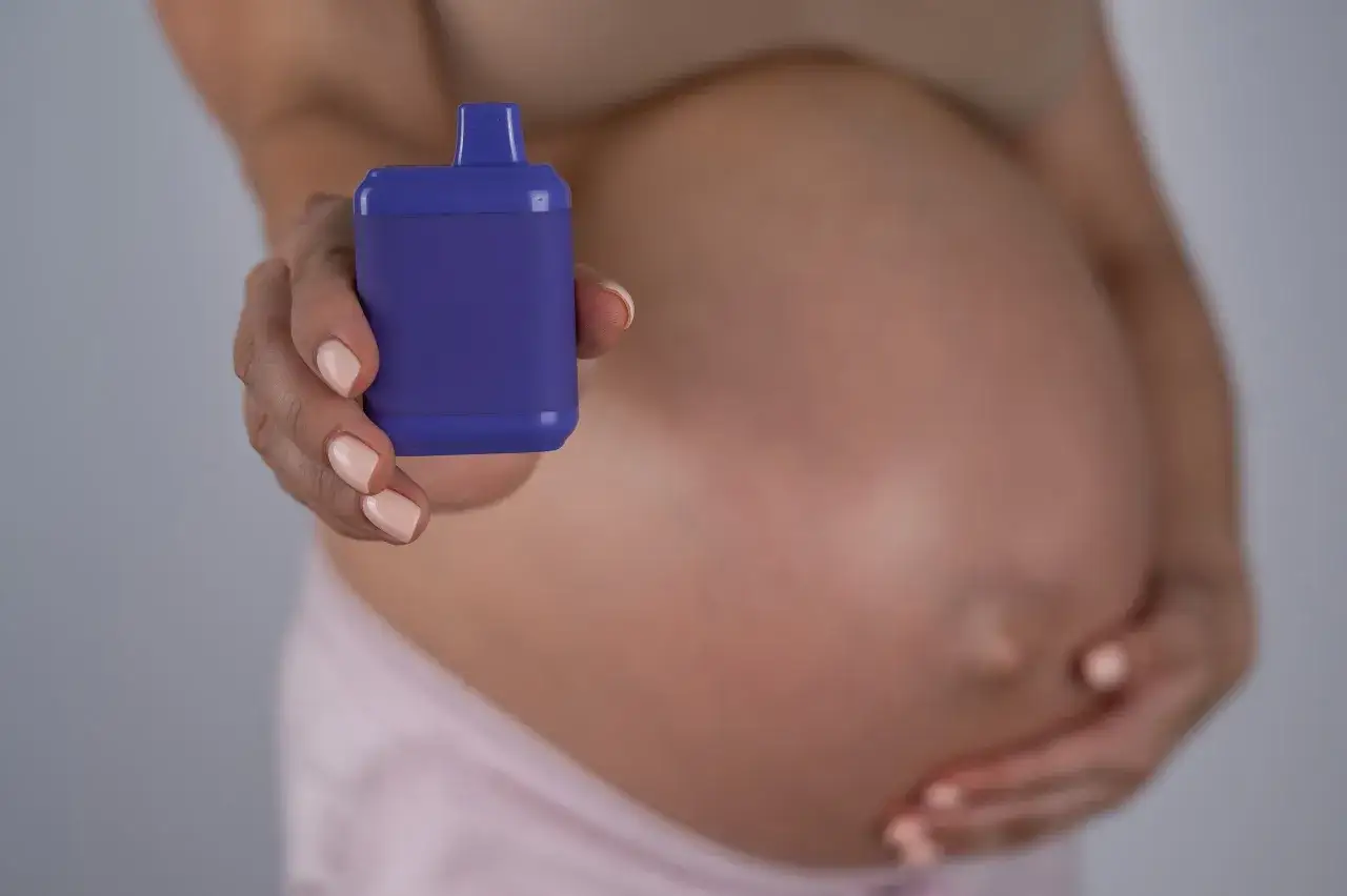 Mujer embarazada sostiene un vapeador morado. Una opci&oacute;n para vapear embarazo sin nicotina.