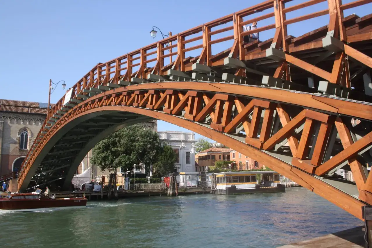 Un ponte in legno a Venezia, uno dei tanti che rendono unica la città. Sotto, un vaporetto naviga sul canale.