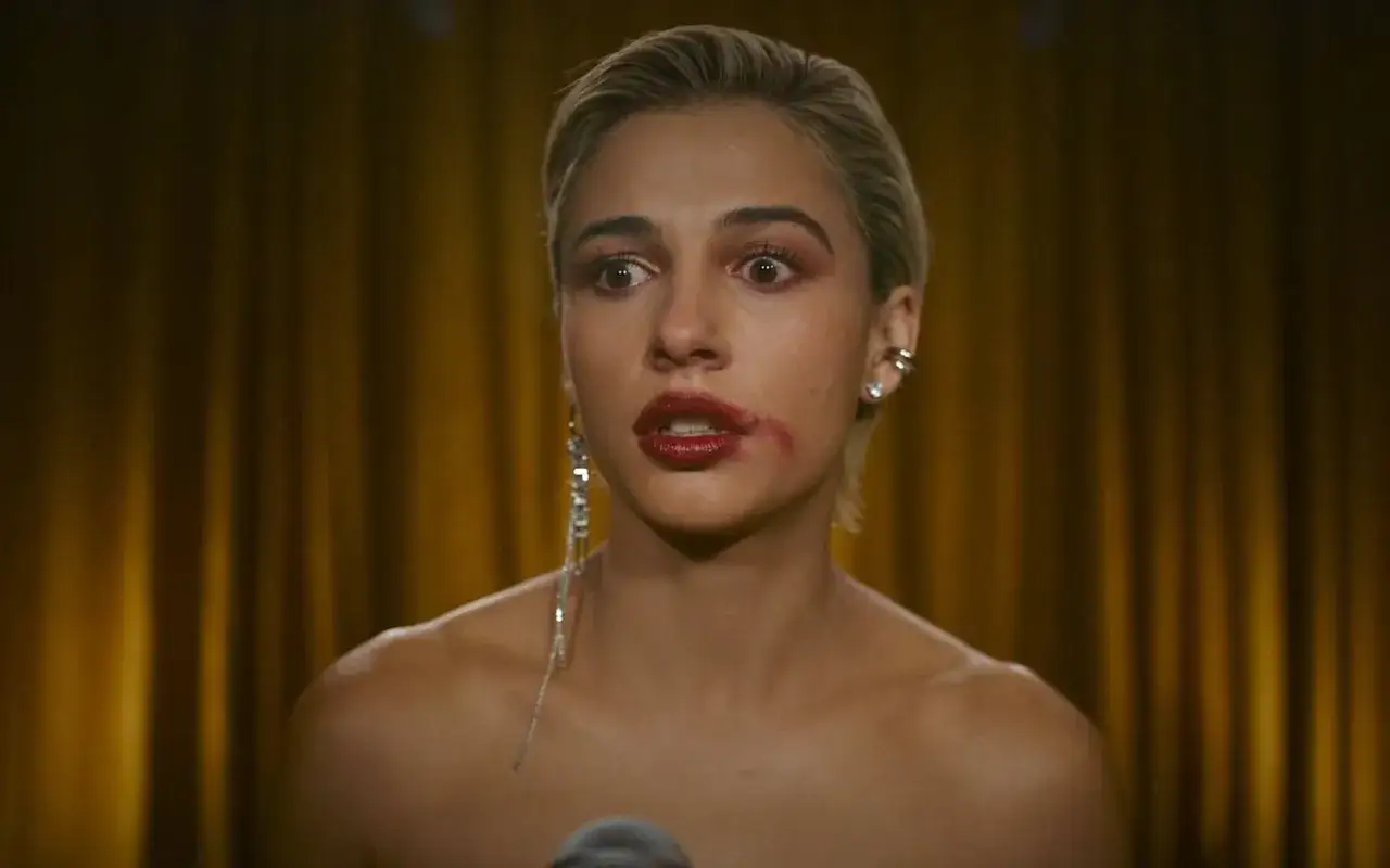 Una mujer con maquillaje corrido y un labial rojo intenso, con una expresión de sorpresa. Su sonrisa parece forzada, casi un rictus.
