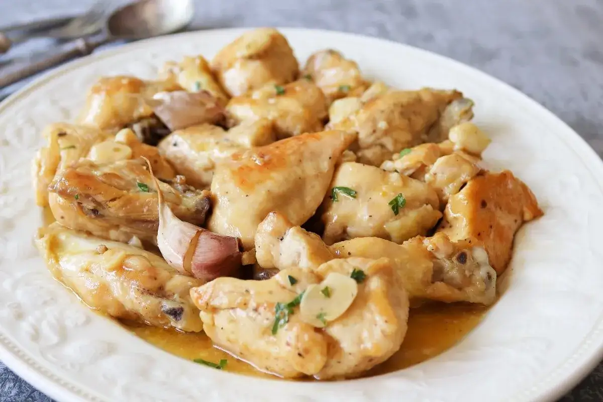 Sabroso pollo al ajillo servido en un plato blanco, con trozos de pollo dorados y jugosos, cubiertos con una salsa de ajo y perejil.